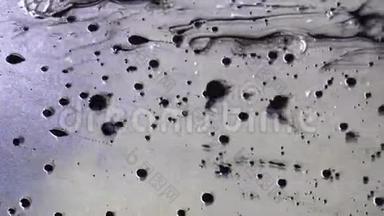 黑色墨水滴在<strong>金属</strong>、灰色背景上的液体油中流动的顶部视图。 黑色的油漆球<strong>漂浮</strong>在